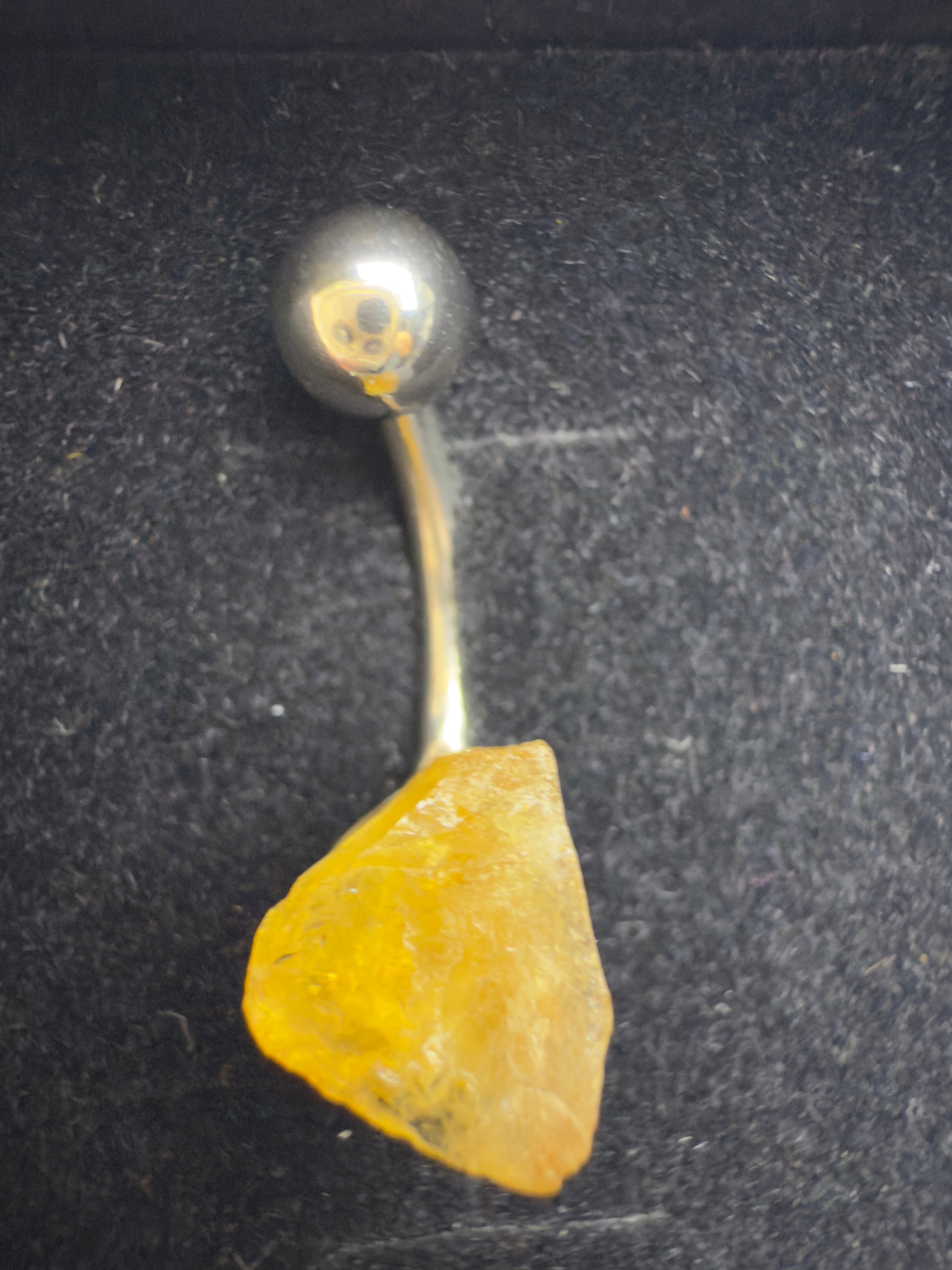 Belly button ring with a yellow stone on a dark background