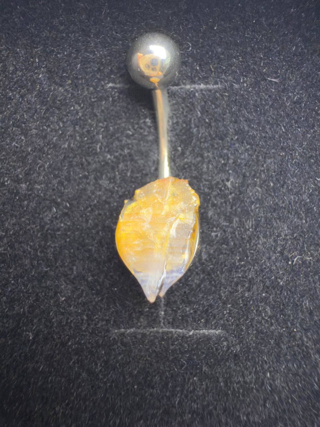 Belly button ring with yellow gemstone on a dark background