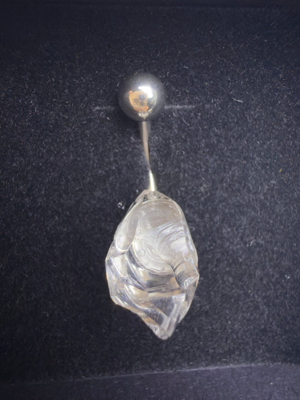 Belly button ring with a clear stone and silver ball on a dark background